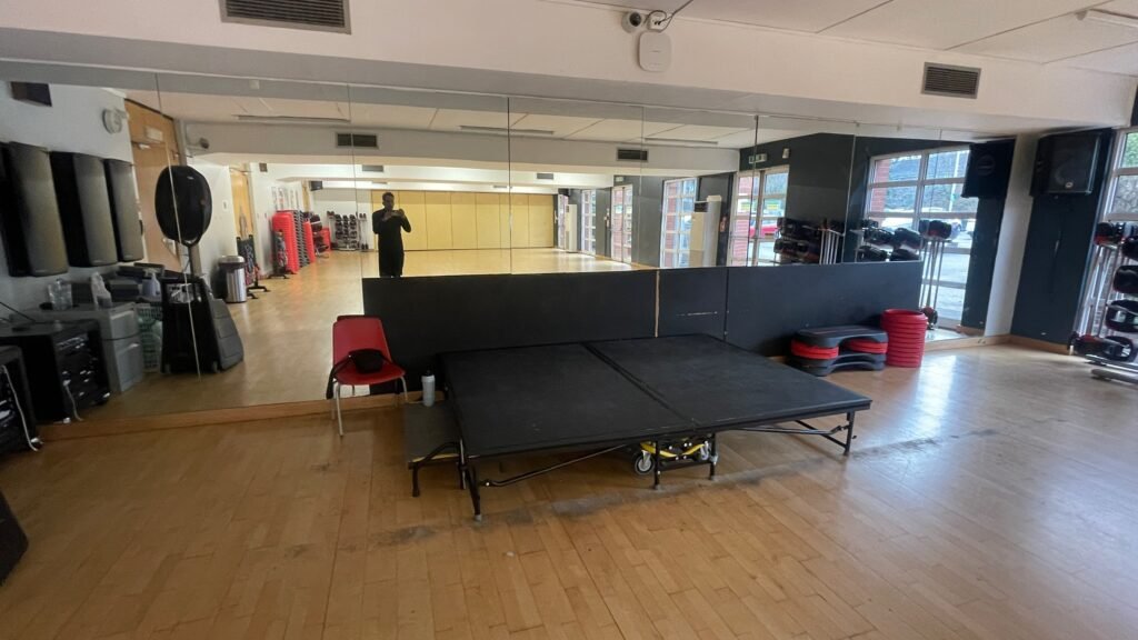 A fitness studio with a stage, with Oz reflected in the mirror